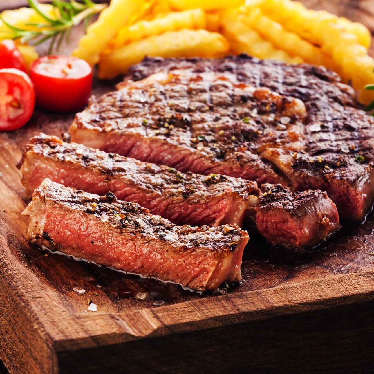 Sliced Steak Ribeye with french fries on serving board block on wooden background